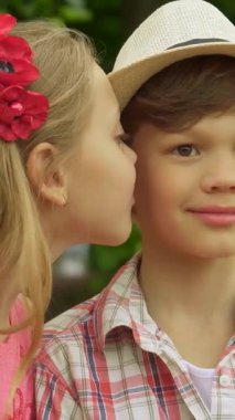 Güneşli bir parkta, sevimli bir kız canlı kırmızı bir bankta tünemiş bir oğlanın yanağını şakayla öpüyor. Neşeli ifadeleri çocukluk masumiyetinin özünü ve yemyeşil ile çevrili tatlı dostluk bağını yakalar.