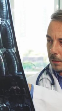 Gıcır gıcır beyaz önlüklü gülümseyen genç bir erkek doktor, iyi aydınlatılmış ofisinde sıcaklık ve profesyonellik saçan bir röntgeni inceliyor. Güneş ışığı geniş pencerelerden süzülerek hasta bakımına olan bağlılığını yansıtan davetkar bir atmosfer yaratıyor.