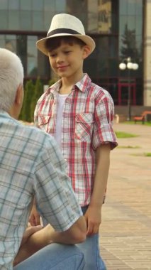 Neşeli bir Kafkasyalı kıdemli adam, neşeli bir parkta büyüleyici torunuyla coşkulu bir beşlik paylaşıyor, neşe saçıyor. Küçük çocuk, modaya uygun bir ekose gömlek ve şık bir şapka ile, yemyeşil ve canlı arasında neşe ile ışıldıyor