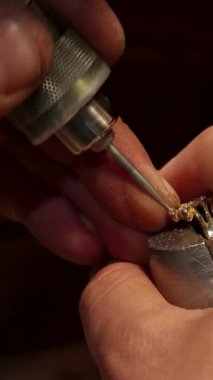 Kendini adamış beyaz bir adam ustalıkla ışıl ışıl bir mücevheri ustalıkla güzel yapılmış bir mücevher parçasına yerleştiriyor ve hassasiyetini ve sanatını sergiliyor. Sabit elleri, aletlerle süslenmiş, mücevher yapımının karmaşık güzelliğini yansıtıyor.