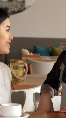 İki hayat dolu kız, bir Asyalı ve bir Kafkasyalı, zarif bir kafe masasında elleriyle kalp şekilleri yaratıyorlar. Buharı tüten beyaz bardaklar ve sıcak bir ortam ile çevrelenmiş olarak, dostluğun ve sevincin özünü somutlaştırırlar, keyifli bir görüntüyü yakalarlar.