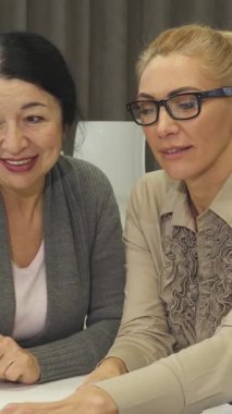 Biri koyu saçlı, diğeri sarışın iki neşeli kıdemli iş kadını, bir dizüstü bilgisayar üzerinde işbirliği yaparken canlı bir tartışma içindeler, pozitiflik ve takım çalışması yayıyorlar. Işıl ışıl gülüşleri ve şık profesyonel kıyafetleri,