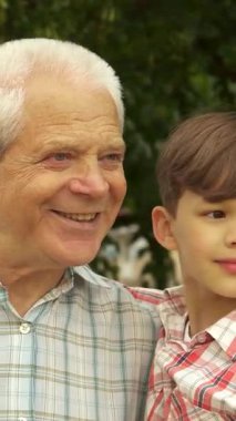 Güneşten sırılsıklam olmuş bir parkta, sevimli küçük bir çocuk, özenli büyükbabasıyla bir sırrı paylaşmak için öne eğilir ve dokunaklı bir bağ anı yaratır. Çekici esmer çocuk, neşeli bir şapkayla süslenmiş, neşe saçıyor.