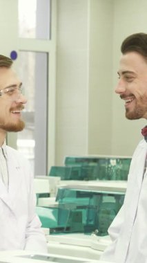 Gösterişli, iyi aydınlatılmış bir laboratuvarda, iki genç erkek asistan güçlü bir bağı yansıtan neşeli ifadeleriyle heyecanlı bir sohbete girişiyor. El değmemiş laboratuvar önlükleri ve koruyucu gözlük giyerek işbirliğinin özüne örnek oluyorlar.