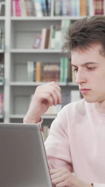 Yumuşak pembe bir kazak giymiş genç bir adam, bir sonraki hamlesini düşünürken dizüstü bilgisayarıyla derinden meşgul, kırsal bir ahşap masada oturuyor. Arkasındaki renkli kitaplıklar sıcak ve davetkar bir atmosfer yaratıyor.