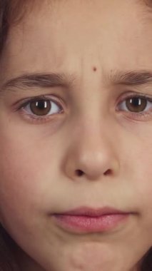 Bu büyüleyici yakın planda kıvırcık saçlı küçük bir kız parmağını nazikçe dudaklarına bastırıyor ve ciddi ama büyüleyici bir ifadeyle sessizlik için işaret veriyor. El değmemiş beyaz arka plan masumiyetini ve merakını vurguluyor.