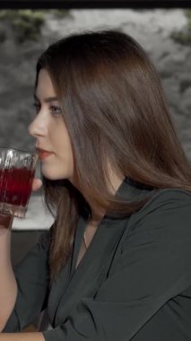 Kamerada uzun, dalgalı saçları olan, şık bir restoran ortamında canlı bir kokteylin tadını çıkaran çekici bir genç kadın. Neşeli ifadesi rahatlama ve kutlama içeriyor. Seyircileri bu keyifli anı paylaşmaya davet ediyor.