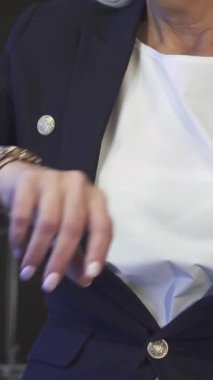 Lüks bir otel odasında, özel dikim ceketli sofistike bir kadın kol saatini aciliyetle kontrol eder. Yumuşak ışığın sıcacık parıltısı kusursuz tırnaklarını ve kendine güvenen duruşunu vurguluyor. Modern çağın özünü somutlaştırıyor.