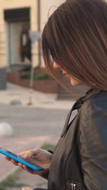 Çekici beyaz bir kız, hareketli bir şehir caddesinde şık bir şekilde alışveriş torbası tutarken kendine güvenen bir şekilde sevinçle ışıldıyor. Akıllı telefonundaki bir numarayı çevirirken neşeli ruhu parlıyor ve gençlik enerjisinin özünü yakalıyor.