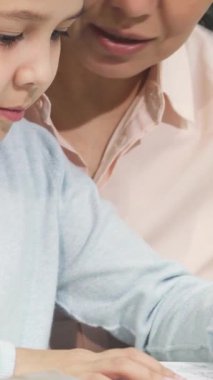 Bu iç açıcı yakın plan ev ödevine dalmış, sevgi dolu annesi yanında gururla ışıldayan küçük bir kızı yakalıyor. Konforlu ev ortamı, öğrenme ve yetiştirme bağının sevincini vurgulayarak sıcaklık ve bağlantı yayıyor.