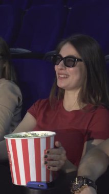 Üç boyutlu şık gözlüklerle süslenmiş iki neşeli çift, sinemanın parlaklığında güneşleniyor, kahkahalarını ve büyük bir kova patlamış mısırlarını paylaşıyorlar. Canlandırılmış gülümsemeleri ve rahat poziyonları canlı bir enerji yayıyor, davetkar bir atmosfer yaratıyor.