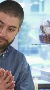 Şık sakallı ve kot pantolonlu, hayat dolu genç bir erkek mağaza asistanı, parlak, hoş geldin pastanesinde baştan çıkarıcı hamur işleri sergileyen bir kadın müşteriyi tutkuyla kendine çekiyor. Neşeli atmosfer, taze pişmiş aromayla dolu.