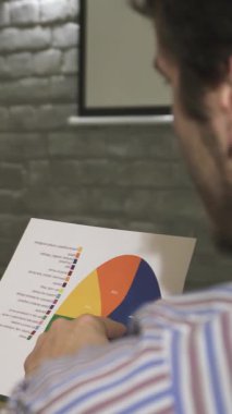 Elinde dumanı tüten bir kahve fincanı tutan enerjik genç bir iş kadını, meşgul edici bir ofis toplantısında erkek arkadaşıyla renkli bir diyagramı enerjik bir şekilde tartışıyor. Atmosfer yaratıcılık ve işbirliği ile elektriklidir.