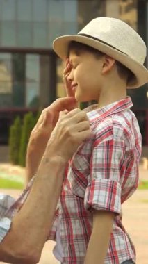 Neşeli, kıdemli bir adam torununu sevgi ve mutluluk saçarak güneşli bir parkta kucaklıyor. Çekici gri saçlı dede, ekose gömlek giymişti. Hoş bir anı paylaşmak için diz çöker. Işıldayan küçük oğluyla, şık bir şapkası olan oğluyla.