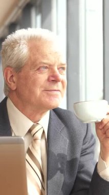 Sivri bir takım elbise ve kravat takmış seçkin bir Kafkas işadamı şık bir kafe masasında sakin bir anın tadını çıkarıyor, pencereden dışarı dikkatlice bakarken kahveyi yudumluyor. Yanında dizüstü bilgisayarı varken modern profesyonelliği somutlaştırıyor.