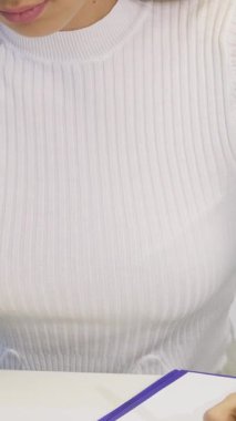 Bu yakın plan çekimde, modern ofis masasında belgeleri doldururken derinden odaklanmış, parlak beyaz kazaklı, çarpıcı bir genç kadın sergileniyor. Işıl ışıl gülüşü ve dengeli tavırları profesyonelliği ve yaratıcılığı yansıtıyor.