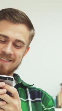 Şık sakallı ve bıyıklı neşeli bir genç adam, parlak, davetkar bir kütüphanede telefonunda mesaj okurken kahkahaya boğuluyor. Etrafı renkli kitaplıklarla çevrili, sıcak gülümsemesi öğrenci hayatının neşesini ve yoldaşlığını yayıyor.