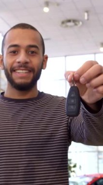 Neşeli bir Afrikalı Amerikalı adam, elinde parlak bir araba anahtarı ile modern, güneşli bir galeride neşe saçıyor. Parlak araçlarla süslenmiş geniş bir ortam heyecan ve hevesli yeni maceralar için hayaller kuruyor.