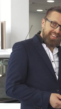 Özel dikim takım elbiseli şık sakallı bir adam şık, modern bir araba galerisinde araba anahtarını gösterirken kendine güvenerek bir telefon görüşmesi yapıyor. Parlak araçlarla çevrili, şık beyaz bir hatchback ve çarpan kırmızı bir araba dahil, heyecan saçıyor.