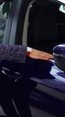 Keskin bir takım elbise giymiş genç bir satıcı, büyüleyici patlıcan renkli bir arabanın parlak yüzeyini sevgiyle okşar, gözleri hayranlıkla parlar. O hevesle kapıyı açarken, lüks iç mekan açılıyor, potansiyel alıcıları içeri davet ediyor.