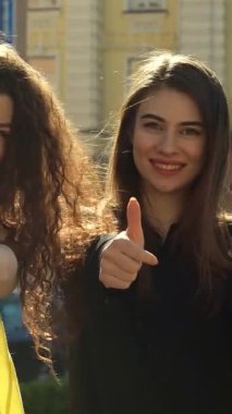 Dalgalı saçları ve ışıl ışıl gülümsemeleri olan iki zarif genç kadın renkli alışveriş torbalarını gururla sergilerken, coşkulu şehir zeminine başparmak sallıyorlar. Bu canlı sahne, arkadaşlığın ve modanın özünü yansıtıyor.