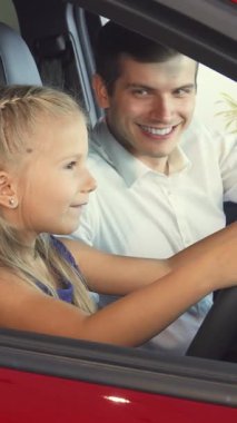 Havada uçuşan sarı saçlı ışıl ışıl küçük bir kız babasının yanında şık kırmızı bir arabada direksiyon sallıyormuş gibi yapıyor. Bulaşıcı gülüşleri ve şakalaşmaları aile neşesi ve bağlantıları için doyurucu bir tablo oluşturuyor.