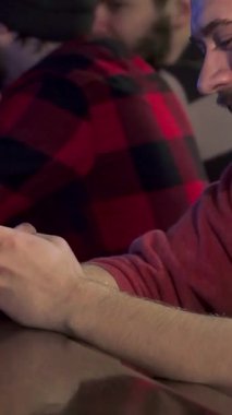 Çekici esmer bir adam akıllı telefonuyla yazarken neşeyle ışıldıyor, hareketli bir barın hareketli atmosferine dalmış. Bar ışıklarının sıcak, davetkar parıltısı şık sakalını ve kareli gömleğini vurguluyor.