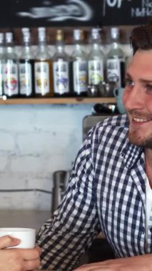 Büyüleyici bir kafede şık bir tişörtü olan genç bir barmen, kahvesinin tadını çıkaran sarışın bir kadınla dinamik bir sohbet eder. Canlandırılmış etkileşimleri sıcak ve davetkar bir atmosfer yaratıyor. Sosyalleşmek ve eğlenmek için mükemmel.