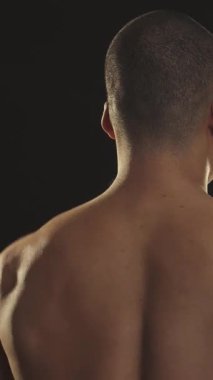 Kaslı bir Afrikalı adamın dikkat çekici dikiz aynası. Kaslarını esnetirken omuzuna kararlı bir bakış atıyor. Dramatik ışıklandırma onun yontulmuş fiziğini, güç ve motivasyonunu vurguluyor.