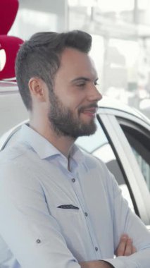 Kendinden emin genç bir adam, çarpıcı yeni otomobilinin anahtarlarını elinde tutarken gururla ışıldıyor, büyük kırmızı bir yayla süslenmiş parlak bir galerinin arka planına kuruluyor. Bu canlı sahne heyecan saçıyor ve yeni bir başlangıcı simgeliyor.