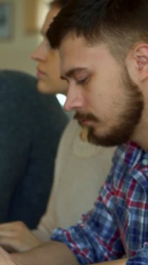 Canlı bir konferans salonunda, kamerada uzun esmer saçlı neşeli beyaz bir kadın, odaklanmış sakallı erkek sınıf arkadaşı notlar alırken. Bu dinamik sahne işbirliği ve coşkunun özünü yakalar.