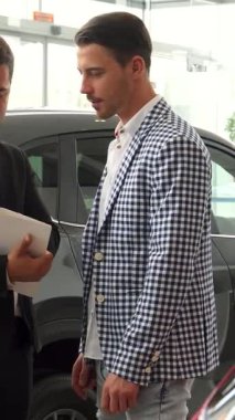 Şık bir araba galerisinde, odaklanmış bir satıcı ayrıntılı bir sözleşme sunarken şık bir spor ceket giyen özenli bir alıcı terimleri yakından inceler. Lüks bir yer edinme konusunda ciddi bir tartışmaya girdiklerinde hava beklentiyle dolup taşıyor.