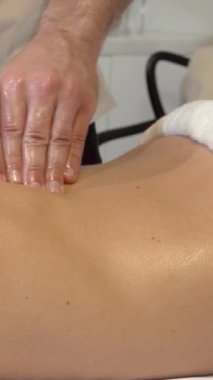 Büyüleyici bir yakın çekim gösterileri yetenekli erkek terapistlerin elleri bir kadının sırtında süzülüyor, parlak yağla kaplanmış, lüks bir kaplıcanın huzurunun tadını çıkarıyor. Yumuşak, ortam aydınlatması ve konforlu çevre davetkar bir ortam yaratır.