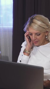 Şık beyaz bir gömlek giymiş ışıl ışıl bir iş kadını, canlı bir telefon görüşmesi yaparken parlak bir dizüstü bilgisayarında zahmetsizce yazı yazarken sevinçle parıldıyor. Yumuşak ışıklandırma ve zarif dekorla süslenmiş şık bir otel odası ilham verici bir şey yaratıyor.