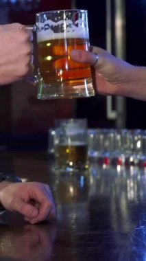 Tarz sahibi, kahverengi saçlı beyaz bir adam barda soğuk bir bira içiyor. Yan profili canlı bir bar atmosferinde rahatlıyor. Yumuşak ışıklandırmanın ve kırsal ahşap aksanların sıcacık parıltısı onu tatmin ederken sarıyor.