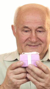 Sıcak gülümsemesi ve gümüş saçı olan mutlu yaşlı bir adam gururla sunar büyüleyici bir şekilde paketlenmiş pembe bir hediye kutusu, neşe ve sıcaklık saçıyor. Bu yürek ısıtan an kutlama ve aşkın ruhunu özetliyor. Aile toplantıları için ideal hale getiriyor.