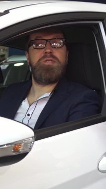 Şık giyimli, sakallı bir adam satış müdüründen arabanın anahtarlarını alırken heyecanla ışıldıyor ve anlaşmayı mühürlemenin heyecanını vurguluyor. Bu canlı sahne, bayiliğin profesyonelliğini ve başarılı olmanın sevincini özetliyor.