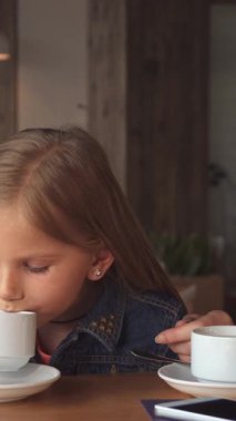 Sıcak ve davetkar bir kafede, uzun sarı saçlı sevimli küçük bir kız annesinin sıcak çay fincanları hakkında anlattığı hoş hikayeyi dikkatle dinliyor. Yumuşak ışıklandırma ve kırsal dekor, neşeli ortamları için mükemmel bir besleyici atmosfer yaratır.