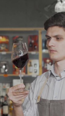 Şık önlüklü şık bir genç adam, davetkar şarap dükkanında bir dizi güzel şişeyle çevrili enfes bir kırmızı şarabın tadını çıkartıyor. Sıcak, kırsal atmosfer tutku ve uzmanlık yayıyor, şarap severleri kendilerini şımartmaya davet ediyorlar.