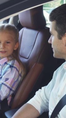 Şık bir arabanın içinde, siyah saçlı genç bir baba büyüleyici bir menekşe elbise giyen kızıyla iç açıcı bir konuşma yapıyor. Neşe dolu değişimleri sıcaklığı ve bağlantıyı yayarak aile sevgisinin özünü modern bir şekilde yansıtıyor.