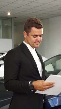 Modern bir araba galerisinde, iki şık giyimli adam bir belgede lüks bir aracın ayrıntılı özelliklerini inceleyerek canlı bir tartışmaya daldılar. Onlar seçenekleri keşfederken atmosfer heyecanla uğulduyor, dinamik dünyayı sergiliyorlar.