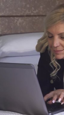 Uçan sarı saçlı dengeli bir kadın lüks otel yatağında rahat bir şekilde, parlak bilgisayarında daktilo ile derinden meşgul. Zarif dekor ve yumuşak ışıklandırma, onun kararlılığını ve profesyonelliğini vurgulayarak sakin bir atmosfer yaratıyor.