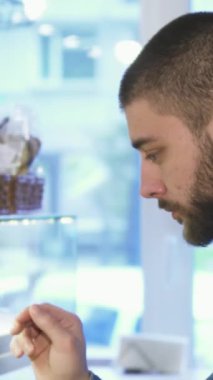 Yakışıklı, sakallı, genç bir adamın yakın çekimi. Fırın vitrinindeki cazip tatlılara bakarken dalgın dalgın dalgın bakıyor. Ağız sulandırıcı hamur işleri ve tatlı ikramlarla dolu canlı görüntü, davetkar bir atmosfer yaratıyor.