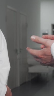 Kendini el değmemiş laboratuvar önlüklü iki erkek doktor, sağlık alanında güven ve işbirliğini simgeleyen sıkı bir tokalaşmayı paylaşıyor. Modern bir hastane koridorunun gösterişli, verimsiz zeminine kurulmuş bu etkili an,