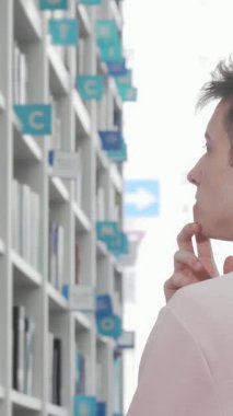 Yakışıklı bir genç adam modern bir kütüphanede düşünceli bir şekilde duruyor. Parmağını çenesinde dinlendirip renkli ve düzenli kitaplıklara bakıyor. Parlak, sakin atmosfer onu edebi bir yolculuğa davet ediyor, merak uyandırıyor ve...