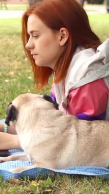 Çarpıcı kızıl saçlı genç bir kız, güneşli bir parkta, sıcak mavi bir battaniyenin üzerinde rahatlar ve dikkatle dizüstü bilgisayarında yazar. Çekici köpeği, tuhaf bir ifadeyle, yakınlarda uzanıyor, arkadaşlığın ve kaygısız yaz günlerinin özünü somutlaştırıyor.