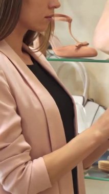 Uzun, dalgalı saçları olan şık bir genç bayan şık bir butikte şık bir bej ayakkabıyı inceliyor, zarafet ve incelik yayıyor. Parlak aksesuarlar ve ayakkabılar ile çevrelenmiş olan sanatçı, sezgilerini sergiliyor.