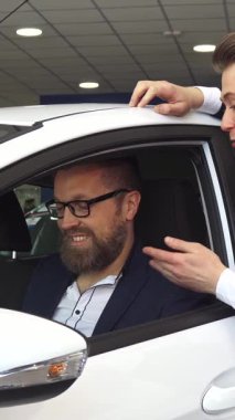 Özel dikim siyah takım elbiseli karizmatik bir satış müdürü galeride parlak beyaz bir arabanın içinde olgun bir beyaz adamla hevesle takılıyor. Canlı gösteri salonu atmosferi, ideal aracı seçmenin heyecanını arttırıyor.