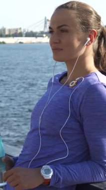 Neşeli genç bir kadın, uzun siyah saçları at kuyruğu içinde, parmaklıklara yaslanıyor ve mp3 çalarının rahatlatıcı seslerinin tadını çıkarıyor. Canlı mor bir bluz giymişti, elinde canlandırıcı bir su şişesi tutuyordu, resimlere karşı mutluluk saçıyordu.