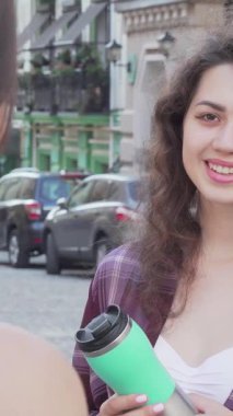 İki neşeli bayan arkadaş büyüleyici bir kaldırım taşı caddesinde ateşli bir sohbete girişiyor, sıcaklık ve bağlantı yayıyorlar. Şık kıyafetleri ve canlı şehir arkaplanı dostluğun özünü yansıtan davetkar bir atmosfer yaratıyor.